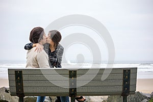 Young biracial couple kissing on bench by the ocean
