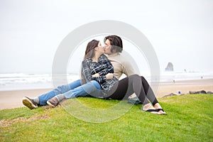 Young biracial couple kissing on grass hill next to ocean