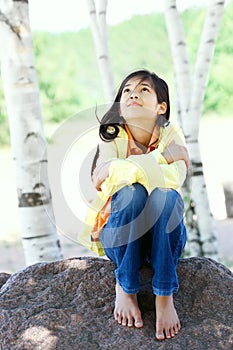 Young biracial girl sitting on rock under trees