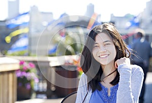 Young biracial teen girl smiling outdoors, sunny background