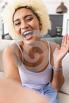 Young biracial woman with curly blonde hair laughs joyfully on video call