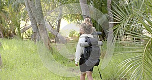 Young biracial woman with curly hair carries a backpack in a lush forest with copy space