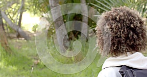 A young biracial woman with curly hair gazes into a lush green outdoor setting with copy space