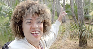 A young biracial woman with curly hair smiles brightly, pointing upwards