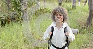 A young biracial woman with curly hair smiles while hiking, with copy space