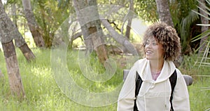 A young biracial woman with curly hair smiles in a lush park setting with copy space