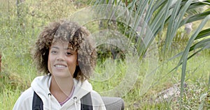 A young biracial woman with curly hair smiles in a natural outdoor setting with copy space