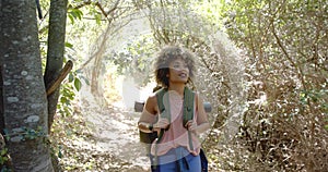 Young biracial woman hikes on a sunny trail, sporting a backpack