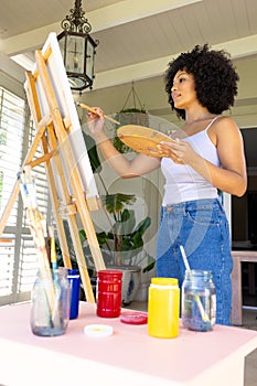 Young biracial woman painting on canvas at home, wearing casual clothes