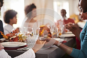 Young black adult woman and her daughter holding hands and saying grace with their multi generation family at the Thanksgiving din