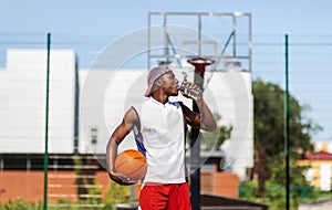 Young black basketball player drinking water to refresh himself after training on outdoor court