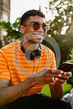 Young black brunette man wearing sunglasses using cellphone outdoors
