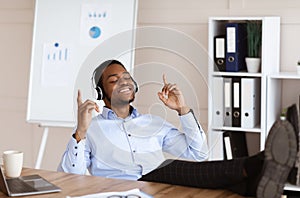 Young black businessman listening to music with legs on table
