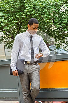 Young black businessman standing on street, looking down at his wristwatch