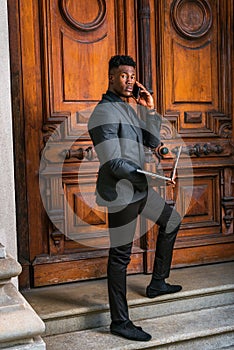 Young black businessman talking on cell phone, working on laptop computer in New York City