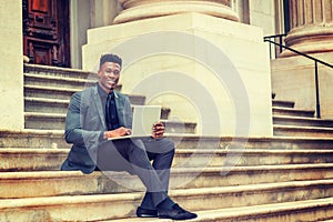 Young black businessman working on laptop computer outside office building in New York City