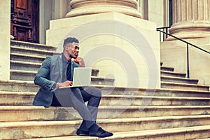 Young black businessman working on laptop computer outside office building in New York City