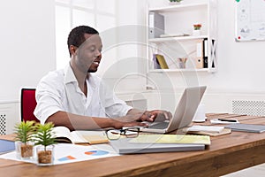 Young black businessman working with laptop in modern white office
