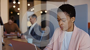 Young black businesswoman with laptop computer and papers working at cozy office. She feeling serious and typing at the