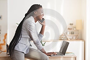 Young Black Businesswoman Talking On Cellphone And Using Laptop In Office