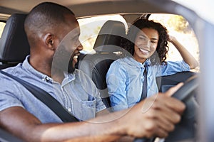 Young black couple in car on road trip smiling at each other