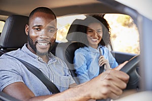 Young black couple in a car on a road trip smiling to camera