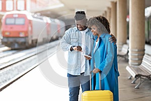 Young black couple checking time on wristwatch while standing at railway station