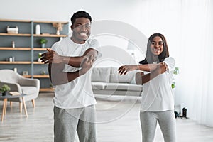 Young black couple doing arm stretch exercise together at home
