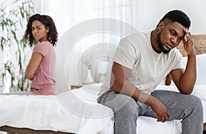 Young black couple having relationships crisis, sitting separated on bed