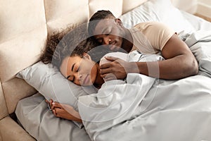 Young black couple hugging sleeping in family bed at home