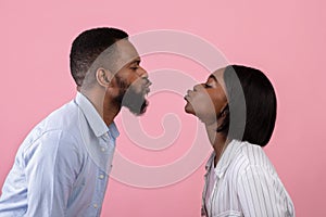 Young black couple in love pursing lips for kiss over pink studio background, side view. Celebrating romantic holiday