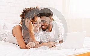 Young black couple lying on bed and using laptop.