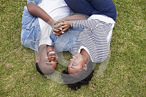Young black couple lying on grass look at each other, aerial