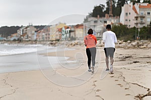 Young black couple in sportswear and wireless headphones run on sea beach, enjoy training