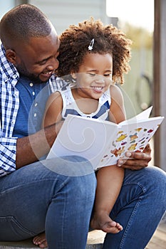 Young black father and daughter reading book outside