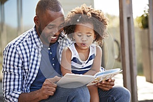 Young black father and daughter reading book outside