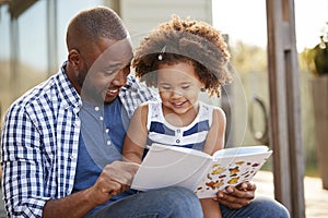 Young black father and daughter reading book outside