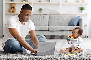 Young Black Father Using Laptop And Taking Care Of Baby At Home