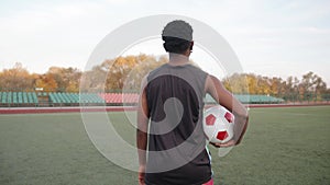 A young black girl goes on a soccer field with a ball in her hand and turns to the camera and smiles