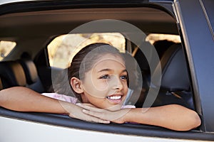 Young black girl looking out of car window smiling, front view