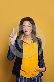 Young black girl pointing up and smiling on colorful yellow background