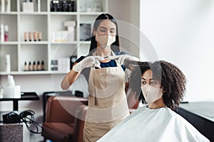 Young black girl in protective mask getting haircut at salon, free space