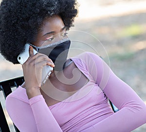 Young black girl wearing protective fabric face mask talking on her cellphone in coronavirus pandemic, COVID-19.