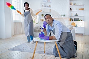 Young black guy feeling tired from housework, his angry wife scolding him for doing nothing, copy space