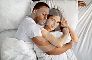 Young black guy sleeping and hugging his beautiful Caucasian girlfriend in bed, top view