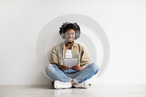 Young Black Guy Wearing Wireless Headphones Relaxing On Floor With Digital Tablet