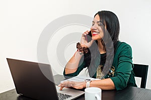 Young black hair woman talking by mobile phone and working at home with the laptop. Teleworking concept on a white background