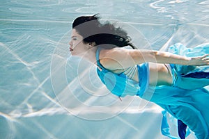 Young black-haired woman in blue dress swims