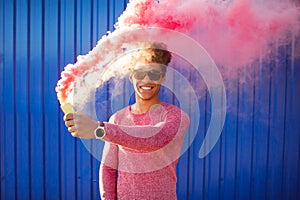 Young black hipster man smiling and holding a colorful pink smoke