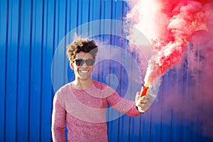 Young black hipster man smiling and holding a colorful pink smoke